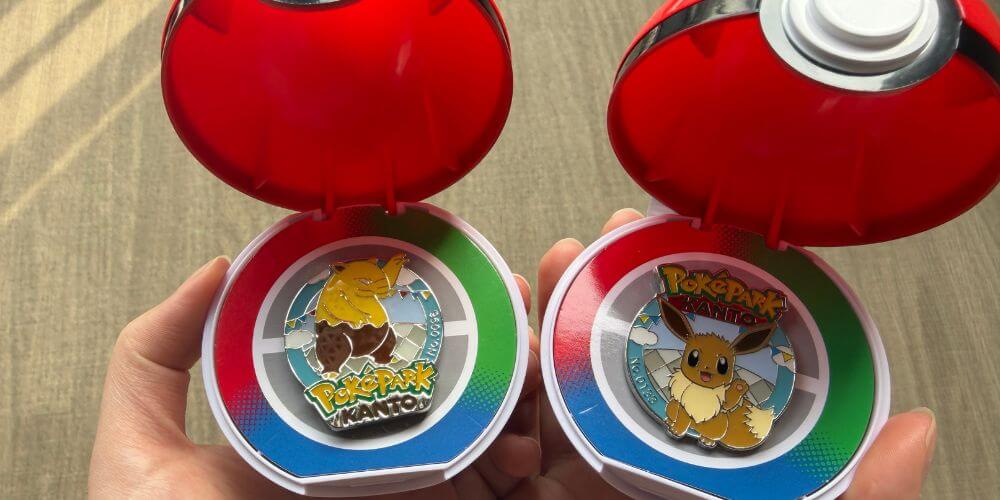 Two open PokeBall capsule toys at PokePark KANTO featuring an Eevee pin and a Drowzee pin held in hand.